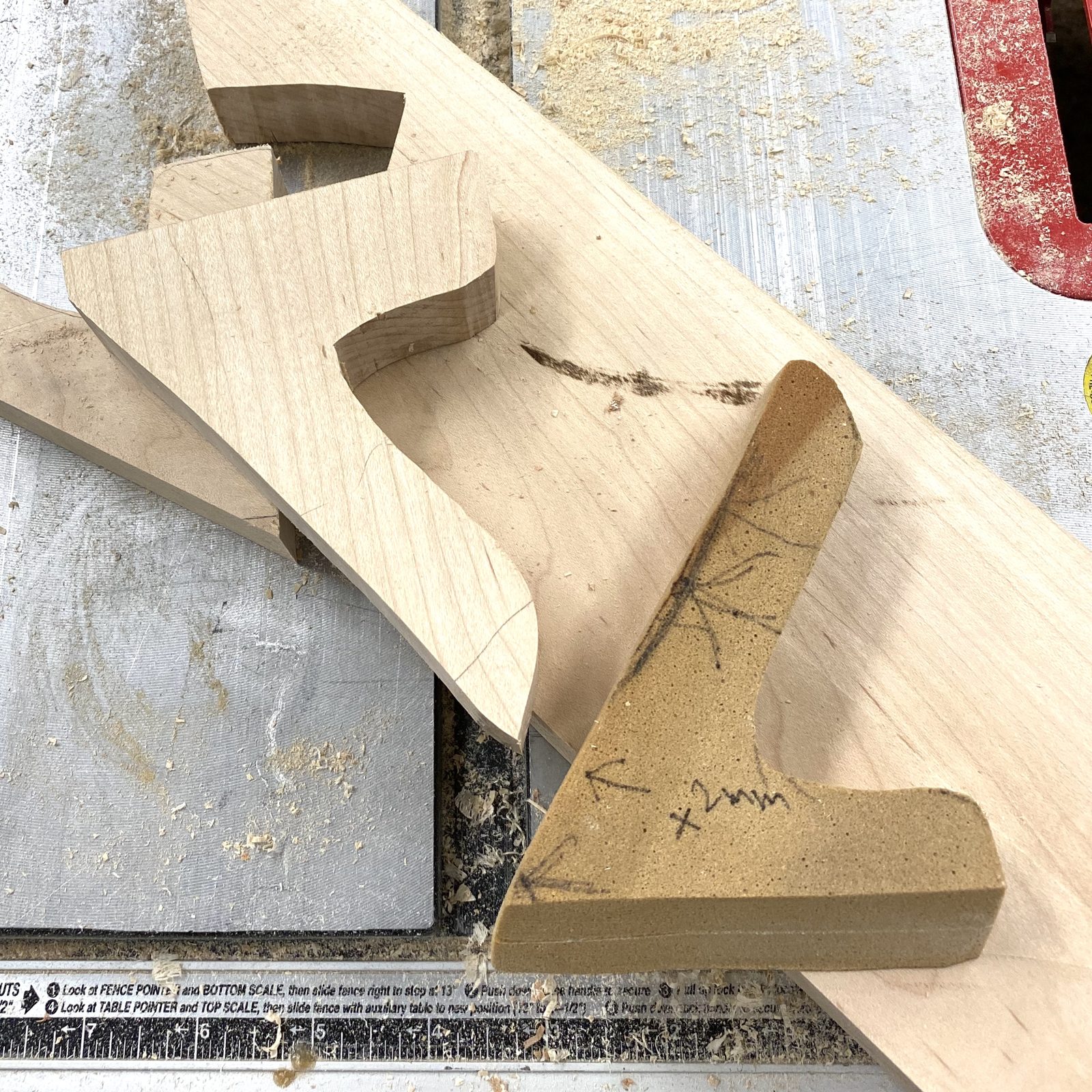 The pattern in balsa foam (the tan piece, penciled with its own notes), beside the finished maple brackets on the saw table. January 2020.