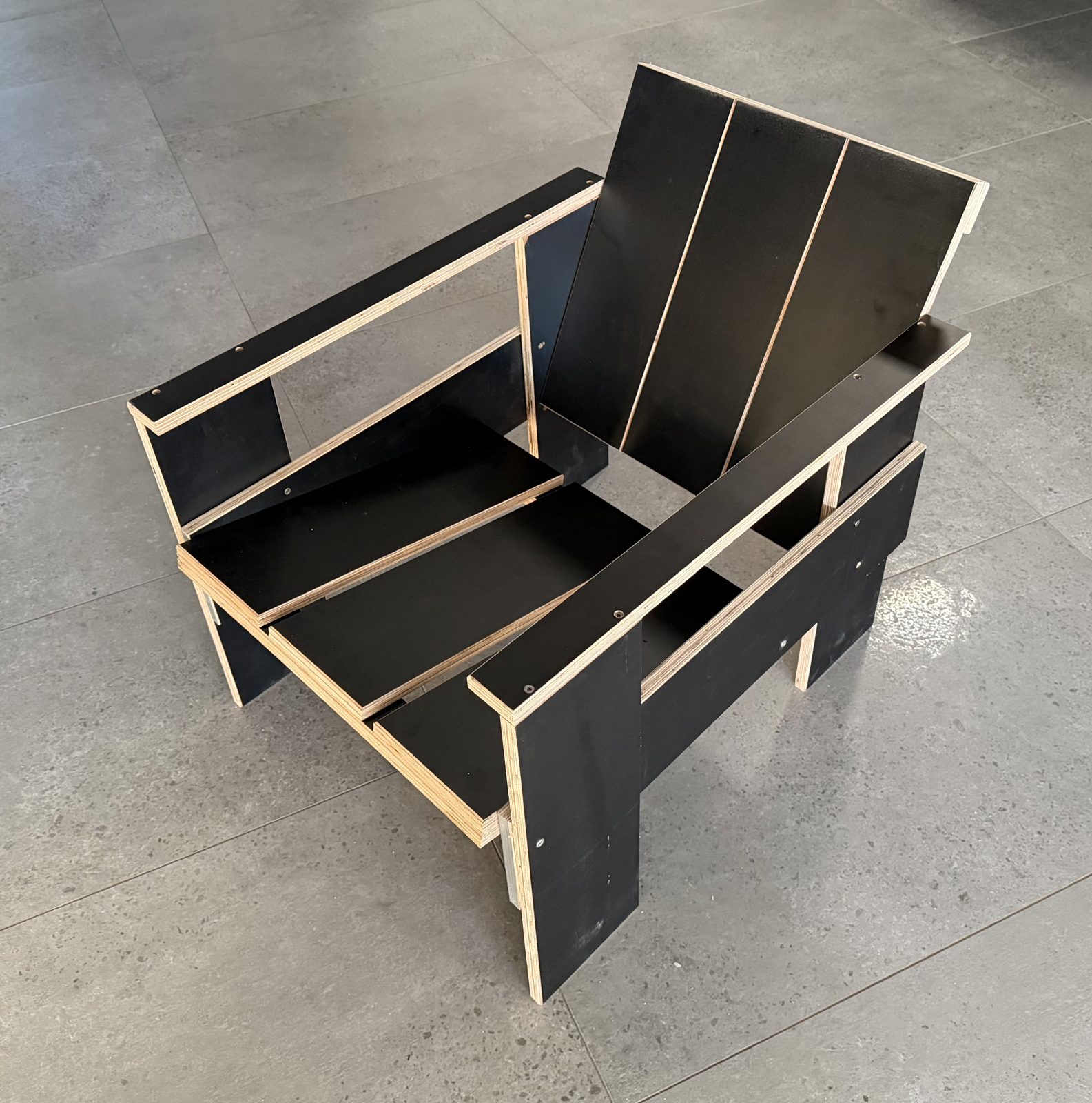 My scrap-plywood replica of Rietveld's 1934 crate lounge, cut from one salvaged sheet of black film-faced plywood, all square cuts. Photographed 30 July 2026.