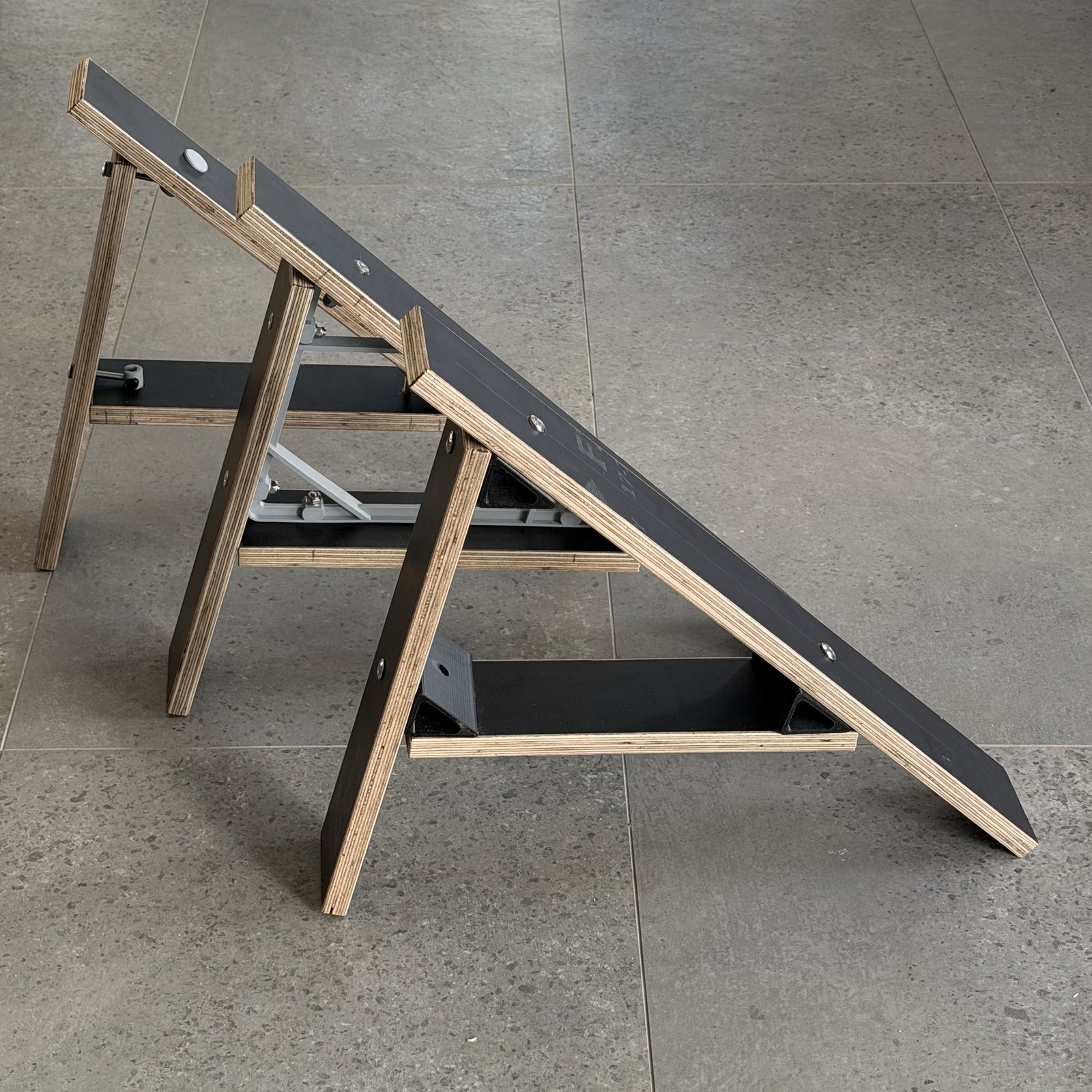 Three K2 side frames standing in a row on tile, each joined at the corners with a different connector: a black printed triangular gusset nearest, a white printed connector, and a metal connector at the back.