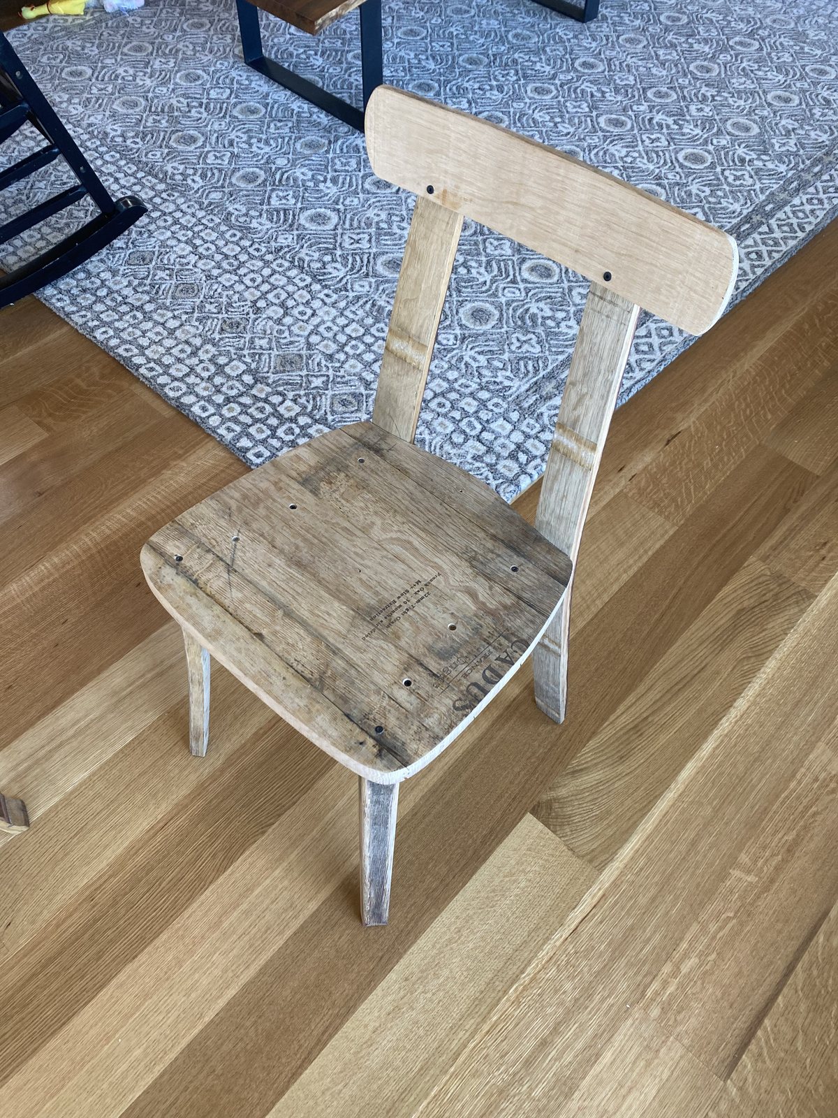 A chair built from reclaimed French oak wine-barrel staves, the seat still showing wine-crate stamps, standing on a wood floor.