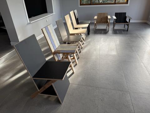 Seven chairs from the project lined up across a tiled room, the black keel chair nearest, two crate lounge chairs at the back