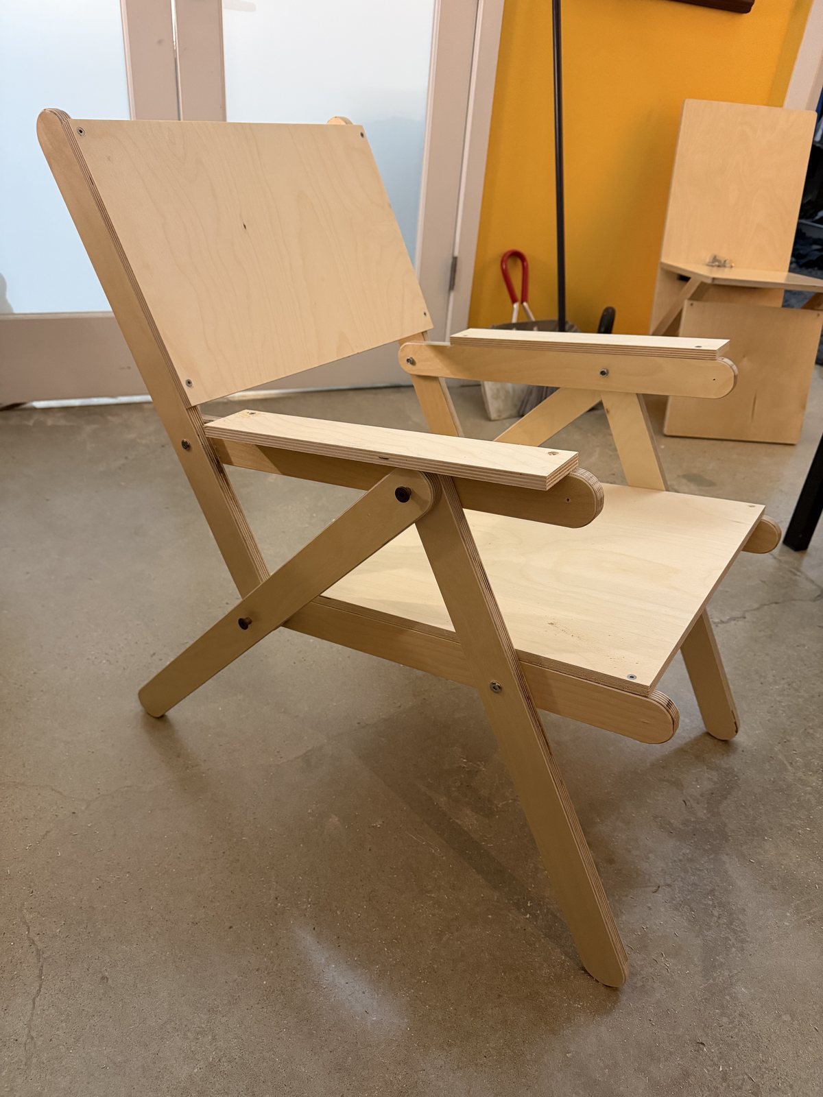 The first K3, the evening it was built: pale birch sticks pinned into two triangles, a single flat back panel, arms, standing on the shop floor.