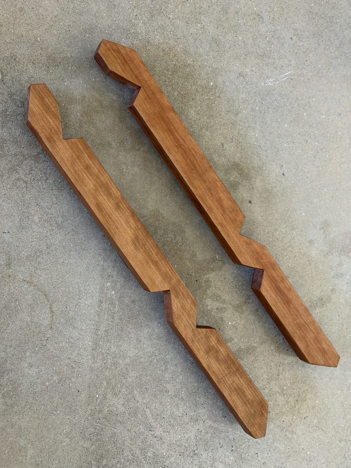 Two cherry keels lying side by side on a concrete floor, cut to shape and finished, each with three fish-mouth notches along its edges and both ends trimmed to a point.
